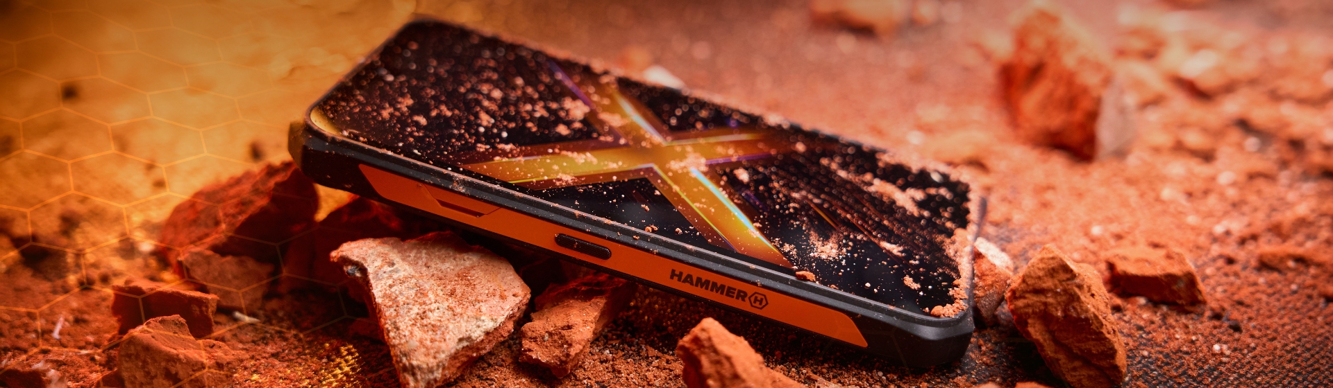 HAMMER ENERGY X2 5G leży na odłamkach skał i pylistej powierzchni, w pomarańczowym świetle, z widocznym ekranem i pancerną obudową