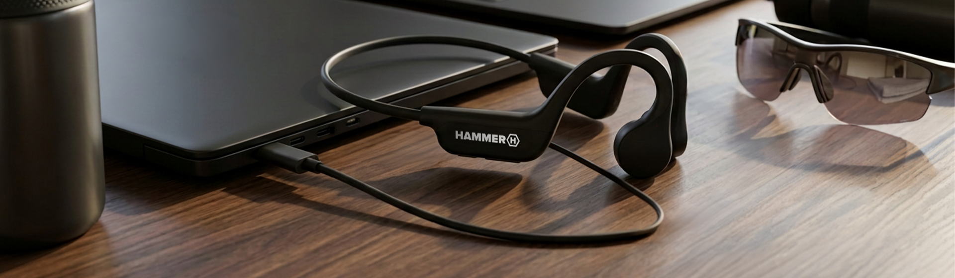 Czarne słuchawki HAMMER BONE HEADPHONES z przewodnictwem kostnym, podłączone przewodem do laptopa na drewnianym biurku