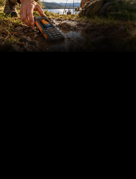 HAMMER LUMEN LTE w czarno-pomarańczowej obudowie zanurzony częściowo w błotnistej kałuży, prezentujący odporność na wodę i trudne warunki