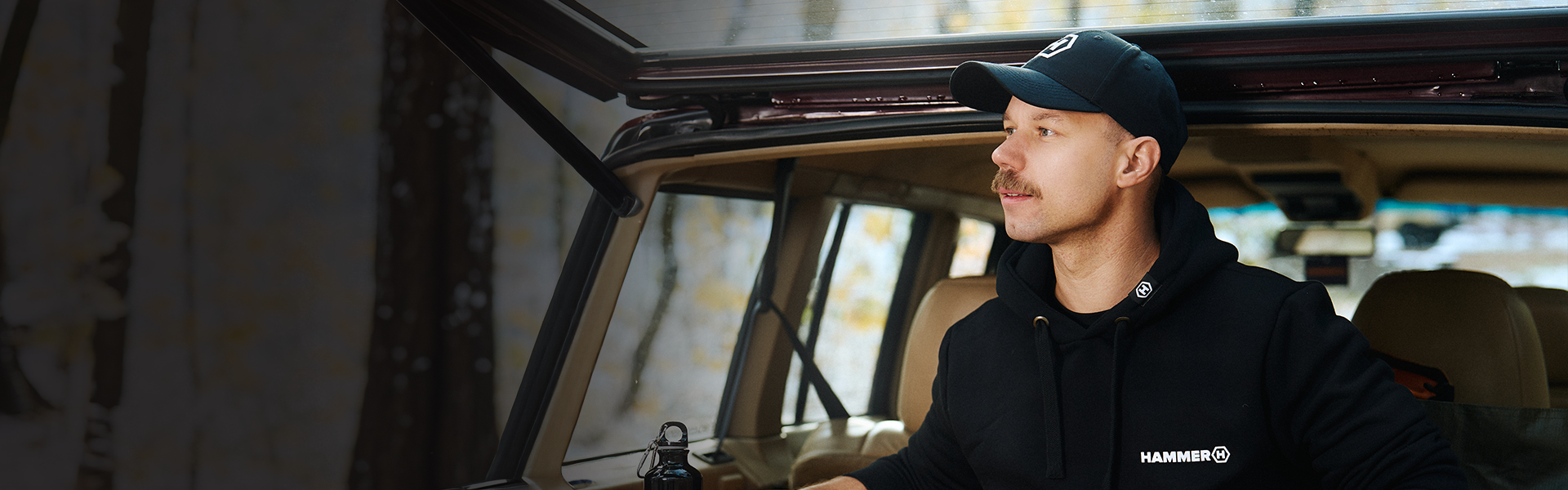 HAMMER CAP czapka z daszkiem idealna na camping las, auto.  Mężczyzna oparty o bagażnik auta. w lesie.