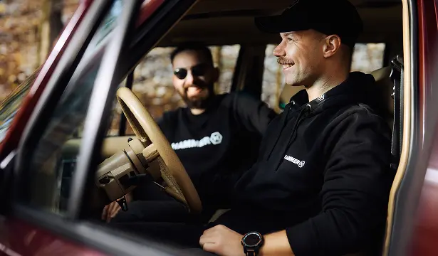 HAMMER HOODIE koledzy siedzą w samochodzie w bluzach HAMMER, śmiejąc się. 