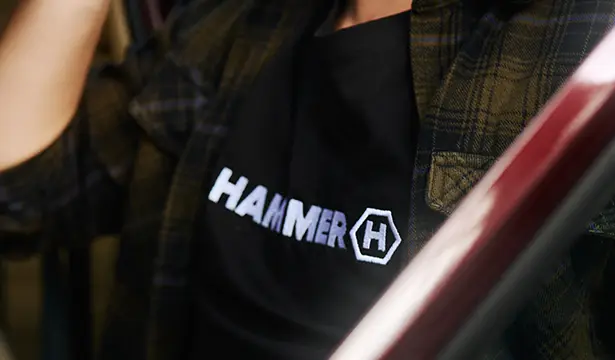 HAMMER T-SHIRT BASIC widok na haftowane logo, podczas wysiadania z samochodu.  Mężczyzna w koszulce HAMMER w kraciastej koszuli. 