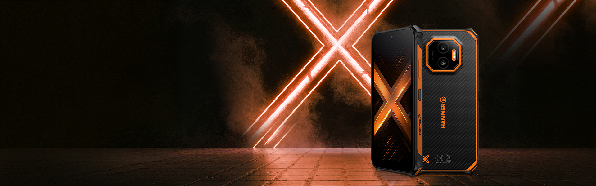 Smartfon HAMMER ENERGY X2 5G na kostce brukowej i na tle neonu z literą X. 