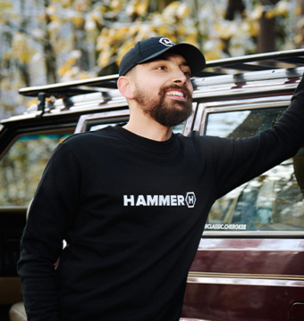 A man leaning against a car, wearing HAMMER WEAR