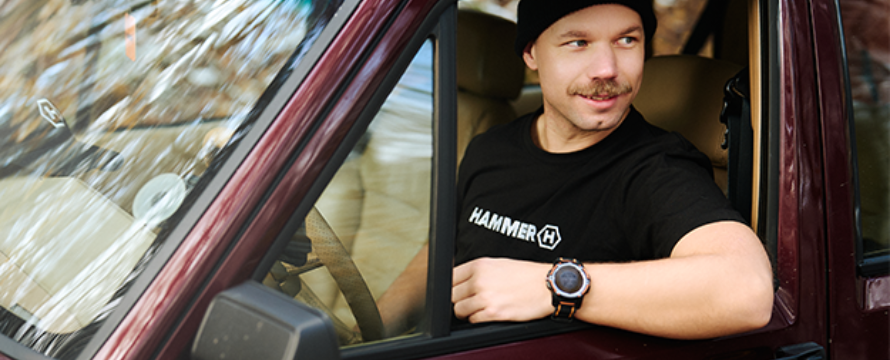 A man is driving a car, wearing HAMMER WEAR.