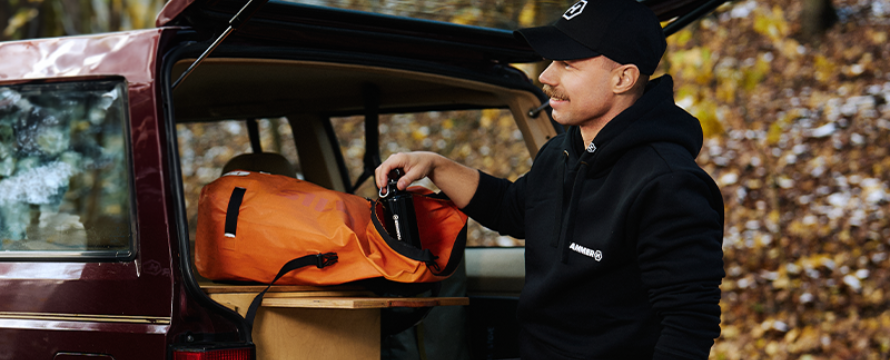 A man standing next to an open car trunk, wearing HAMMER WEAR