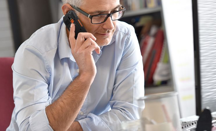 HAMMER 6 LTE mężczyzna w niebieskiej koszuli, w średnim wieku rozmawia przez telefon klasyczny w biurze.