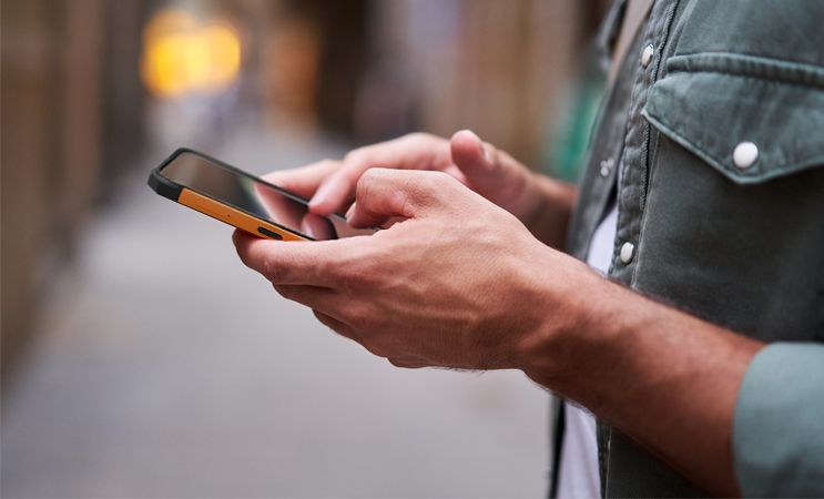 HAMMER IRON Va mężczyzna trzyma telefon w ręku., ma zieloną koszulę.